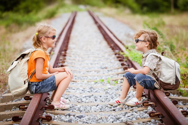 Двое маленьких детей с рюкзаком сидят на железной дороге — стоковое фото