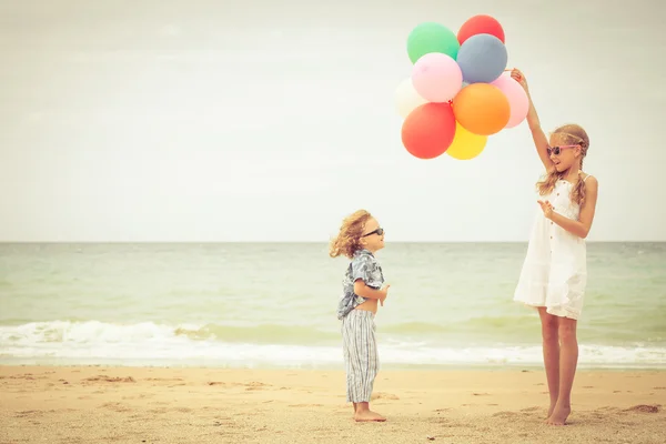 Два маленьких ребенка с воздушными шарами, стоящими на пляже — стоковое фото