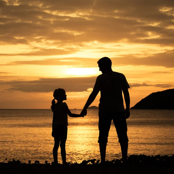 Far och dotter står på stranden vid solnedgången tid. — Stockfoto