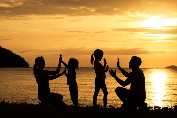 Silueta de familia feliz que juega en la playa al atardecer — Foto de Stock