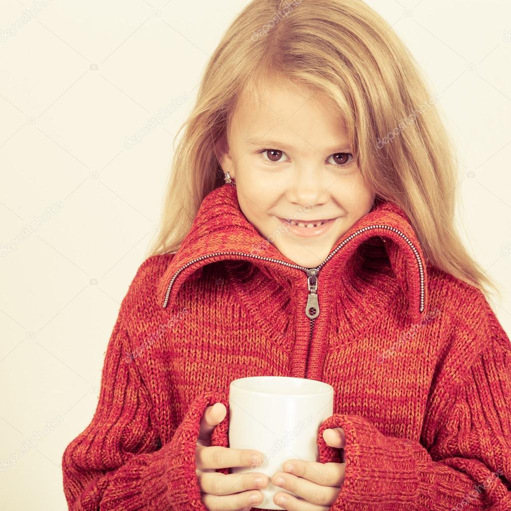 portrait of a cute little girl in red sweater holding a mug in h