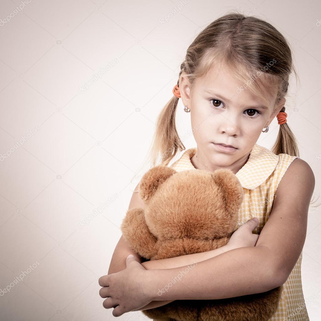 Portrait of sad blond little girl standing near wall 