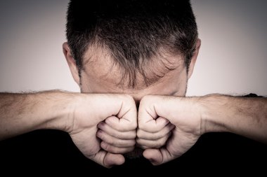 Duvarın yanında duran üzgün bir adamın portresi. Yüzünü kapatıyor.