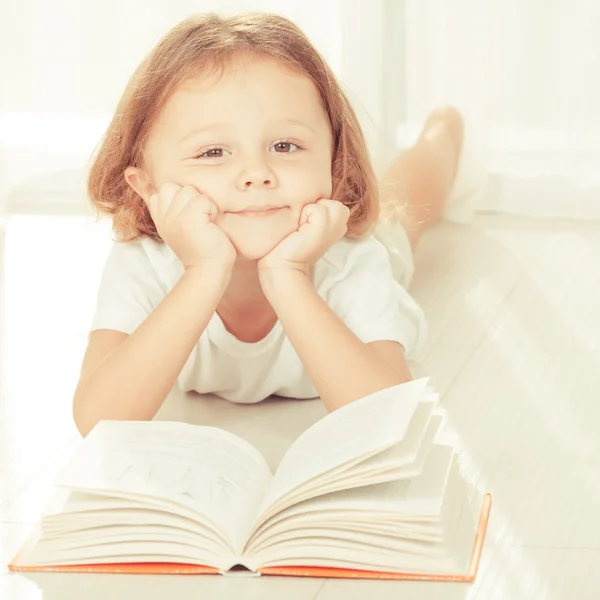 Little child reading book  lying down on floor — Stock Photo, Image