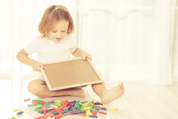 Kleine jongen spelen met houten mozaïek op de vloer — Stockfoto