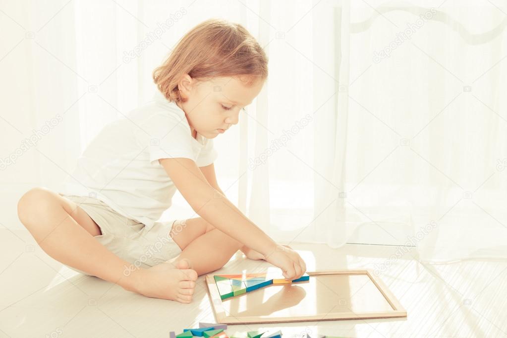 little boy playing with wooden mosaic on the floor