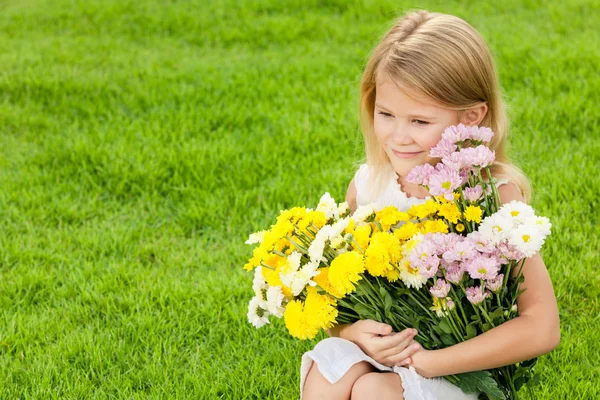 Een gelukkig meisje, zittend op het gras met een boeket van flo — Stockfoto