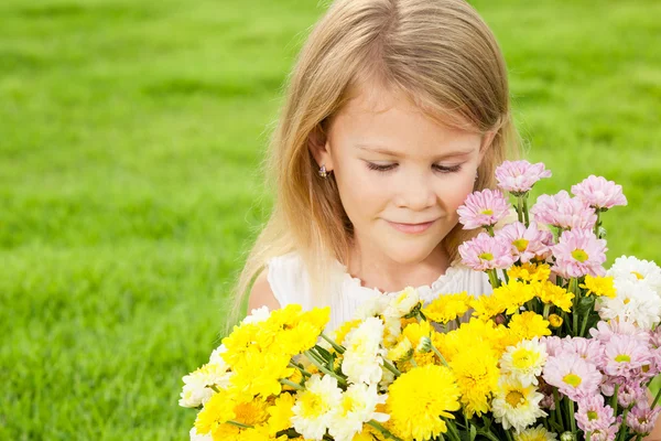Ein glückliches kleines Mädchen sitzt auf dem Gras mit einem Blumenstrauß — Stockfoto