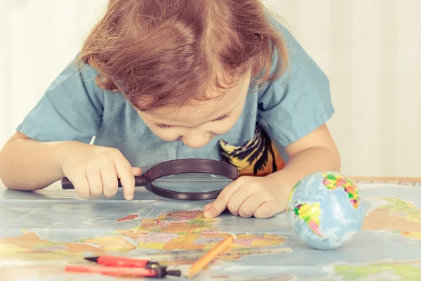 Bambino considerando una mappa del mondo con una lente d'ingrandimento — Foto Stock