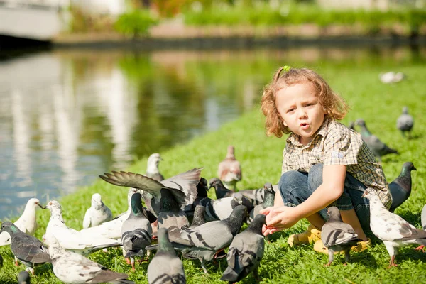 Küçük çocuk parkta güvercinleri besliyor.
