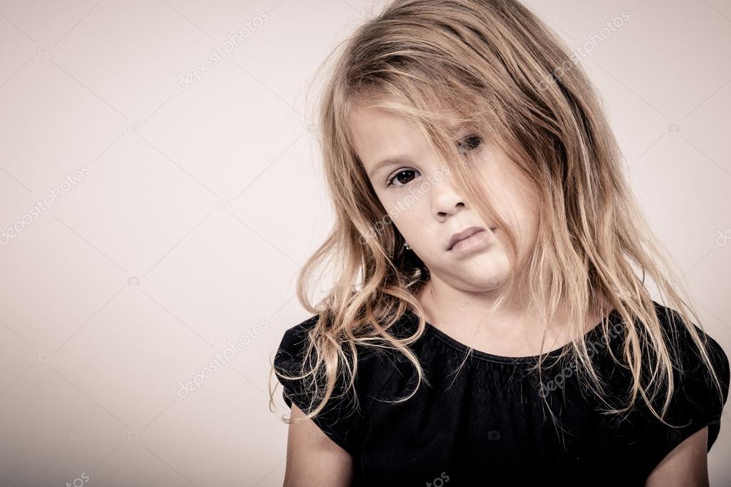 Portrait of sad blond little girl standing near wall