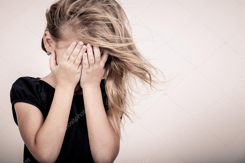 Portrait of sad blond little girl standing near wall