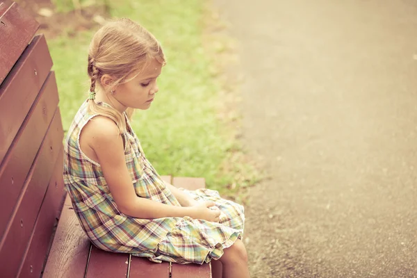 Sad little girl sitting on bench in the park at the day time — Stock Photo, Image