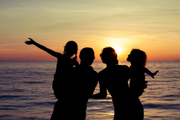 Silhouette einer glücklichen Familie, die am Strand in der Sonne spielt — Stockfoto