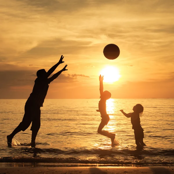 Pai e crianças brincando na praia na hora do pôr do sol . — Fotografia de Stock