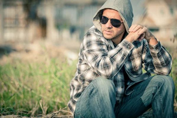 Portrait of a sad man in sunglasses sitting near the house