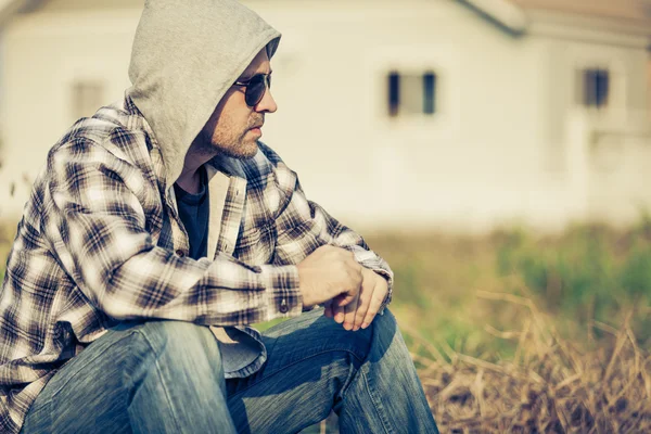 Portrait of a sad man in sunglasses sitting near the house — Stock Photo, Image