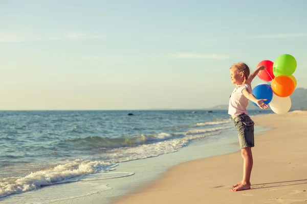 Маленькая девочка с воздушными шарами, стоящими на пляже — стоковое фото