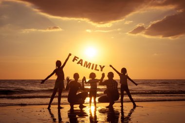 Happy family standing on the beach at the sunset time.  clipart