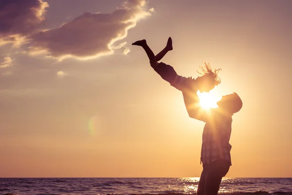 Far och son som spelar på stranden vid solnedgången tid. — Stockfoto