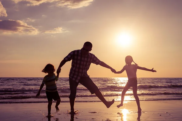 Pai e crianças brincando na praia na hora do pôr do sol . — Fotografia de Stock