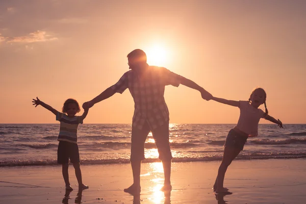 Pai e crianças brincando na praia na hora do pôr do sol . — Fotografia de Stock