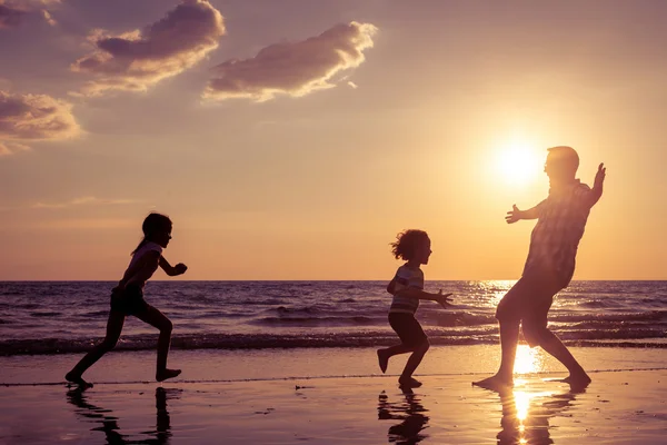 Pai e crianças brincando na praia na hora do pôr do sol . — Fotografia de Stock