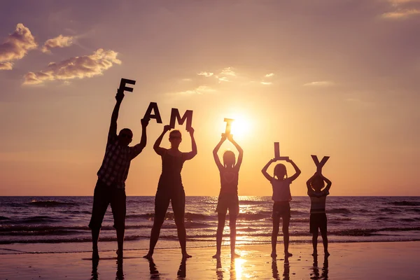 Familia feliz de pie en la playa al atardecer . — Foto de Stock