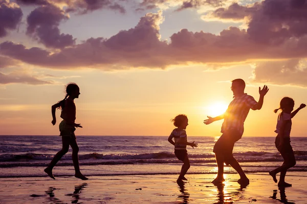 Vader en kinderen spelen op het strand op de zonsondergang keer. — Stockfoto