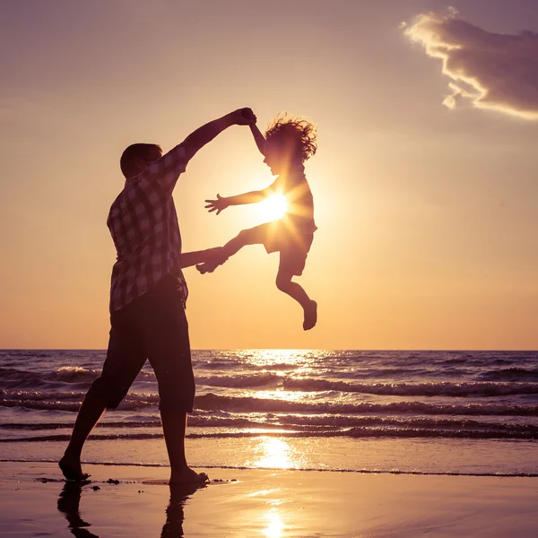 Pai e filho brincando na praia na hora do pôr do sol . Imagens Royalty-Free