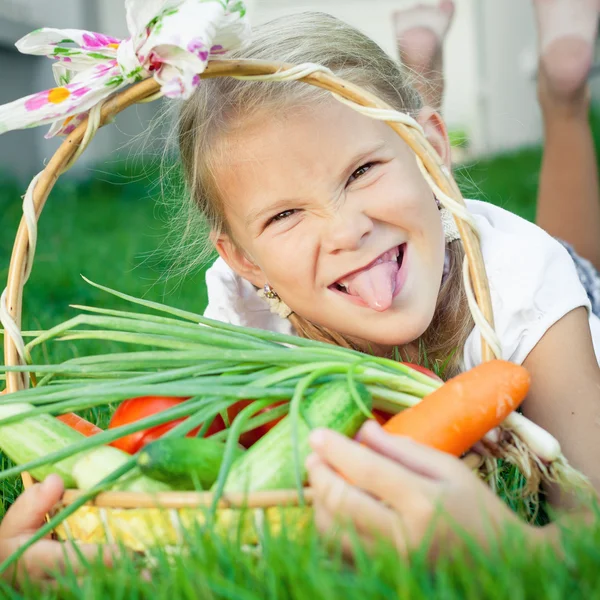 Bonne petite fille allongée sur l'herbe avec un panier de légumes — Photo