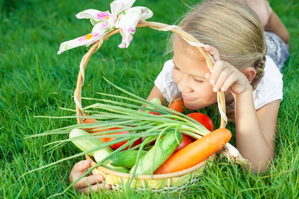 Bonne petite fille allongée sur l'herbe avec un panier de légumes — Photo