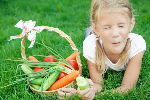 Щаслива маленька дівчинка лежить на траві з кошиком з овочів — стокове фото