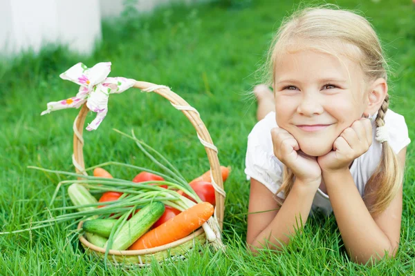 Щаслива маленька дівчинка лежить на траві з кошиком з овочів — стокове фото