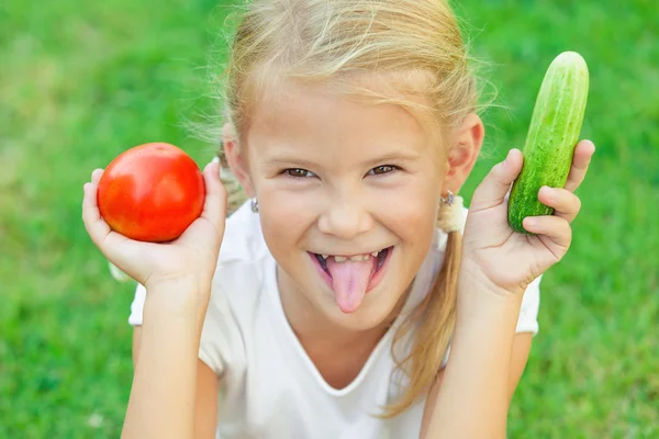 Happy little girl sitting on the grass with a vegetables at the — Stock Photo, Image