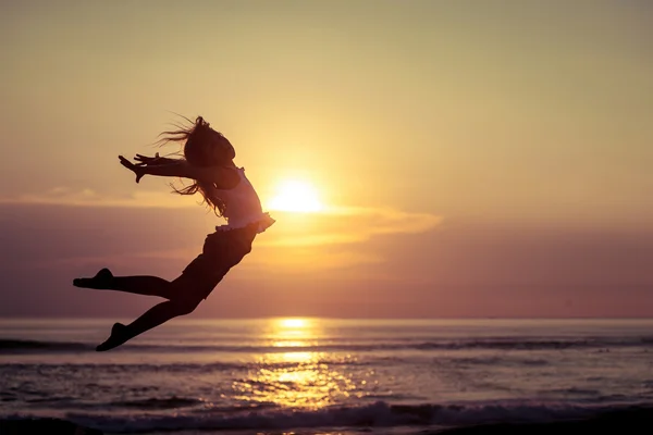 Menina feliz pulando na praia na hora do pôr do sol — Fotografia de Stock