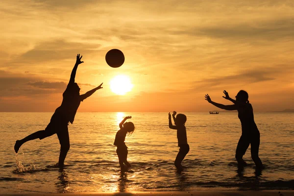 Silhuett av en lykkelig familie som leker på stranden ved soloppgang. – stockfoto
