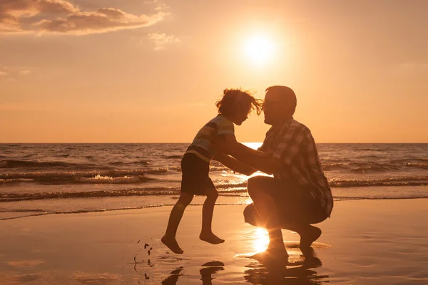 Far och son som spelar på stranden vid solnedgången tid. — Stockfoto