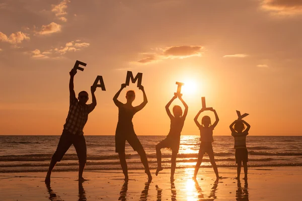 Família feliz em pé na praia na hora do pôr do sol . — Fotografia de Stock