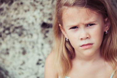 Portrait of sad blond little girl sitting on the beach