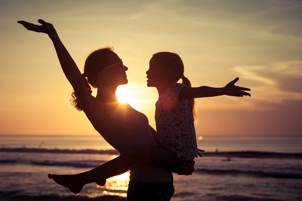 Mor och dotter spelar på stranden vid solnedgången tid. — Stockfoto
