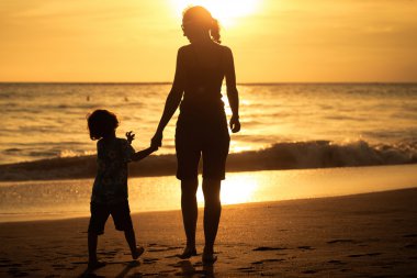 Mother and son playing on the beach at the sunset time. clipart