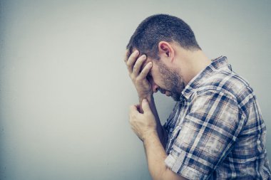 Duvarın yanında duran üzgün bir adamın portresi. Yüzünü kapatıyor.