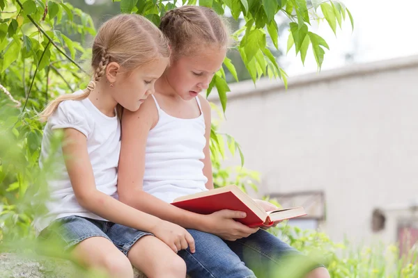 Twee kleine meisjes met boek zit in het park — Stockfoto