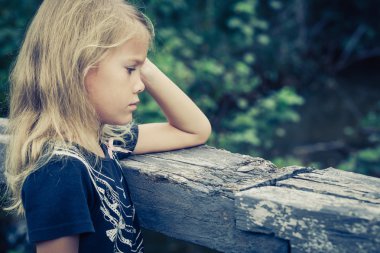 Portrait of sad blond little girl sitting on the bridge