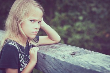 Portrait of sad blond little girl sitting on the bridge