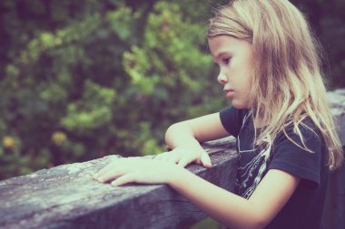 Portrait of sad blond little girl sitting on the bridge