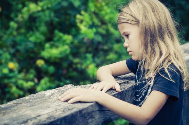 Portrait of sad blond little girl sitting on the bridge