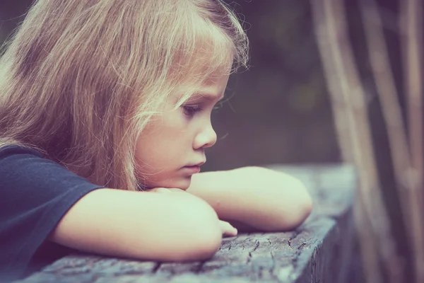 Portrait of sad blond little girl sitting on the bridge — Zdjęcie stockowe