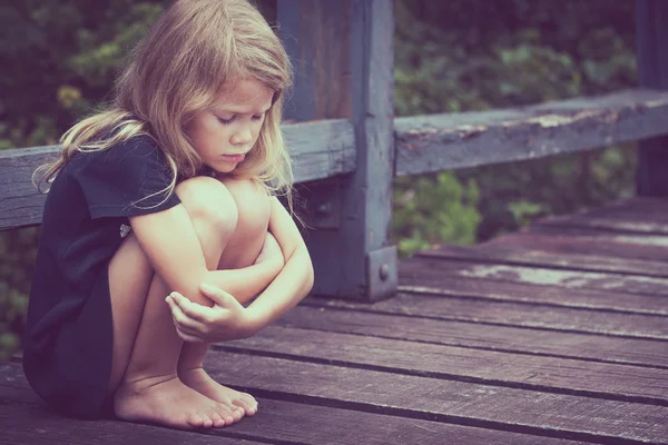 Portrait of sad blond little girl sitting on the bridge — Stock Photo, Image